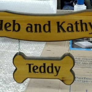 May include: Wooden sign with the names "Heb and Kathy" on a banner and "Teddy" on a bone-shaped plaque.