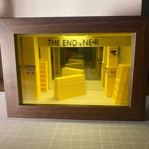 May include: A shadow box with a dark wood frame containing a yellow miniature diorama of a room. The text THE END IS NEAR is printed above. The scene features yellow pillars, shelving units, and small warning signs with icons, all set against a mirror.