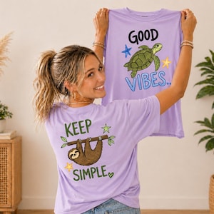 May include: A light purple t-shirt with the words "Good Vibes" and a cartoon turtle on the front. The back of the shirt has a sloth hanging from a branch with the words "Keep Simple".