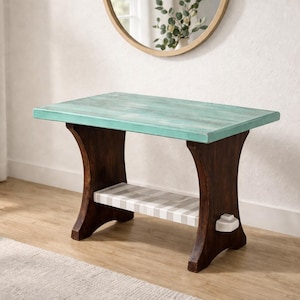 May include: A small wooden side table with a rectangular top and curved legs. The tabletop is painted a distressed teal colour, while the legs are a dark brown. A shelf with a grey and white striped pattern is located between the legs.
