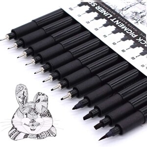May include: A set of black pigment liner pens with varying tip sizes. The pens are arranged in a row, with a white and black ruler-like card on top. A black and white illustration of a rabbit is on the left.
