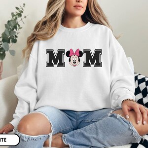 May include: White sweatshirt with the word "MOM" in black block letters, with a Minnie Mouse graphic in the center. Minnie Mouse is wearing a pink bow. The sweatshirt is a crew neck style.