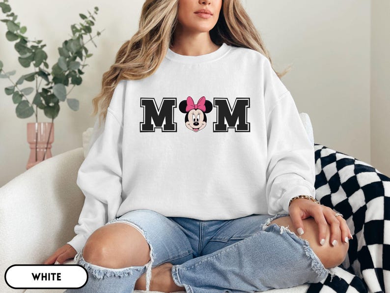 May include: White sweatshirt with the word "MOM" in black block letters, with a Minnie Mouse graphic in the center. Minnie Mouse is wearing a pink bow. The sweatshirt is a crew neck style.