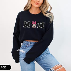 May include: Black sweatshirt with the word "MOM" in white block letters, with a Minnie Mouse graphic in the center. The Minnie Mouse graphic has a pink bow. The word "BLACK" is in a black rectangle at the bottom.