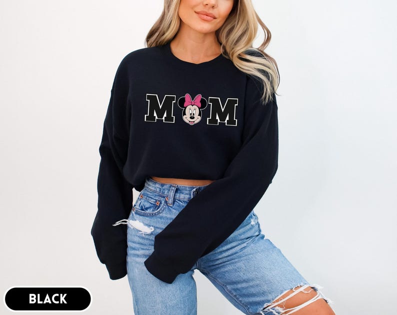 May include: Black sweatshirt with the word "MOM" in white block letters, with a Minnie Mouse graphic in the center. The Minnie Mouse graphic has a pink bow. The word "BLACK" is in a black rectangle at the bottom.