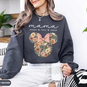 May include: Dark gray heather sweatshirt with the word "mama" in script. Below the word "mama" are the names Nathan, Chole, and Jordan. The sweatshirt features a floral Mickey Mouse head design with a pink bow.
