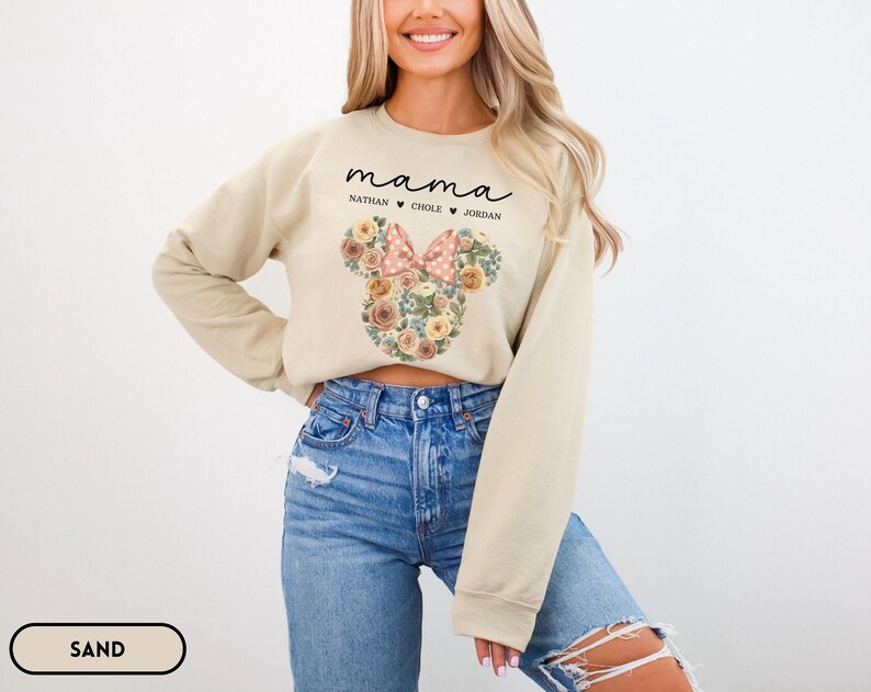 May include: A sand-colored sweatshirt with the word "mama" in black script above the names Nathan, Chole, and Jordan. A floral Minnie Mouse head design with a pink bow is centered on the front.
