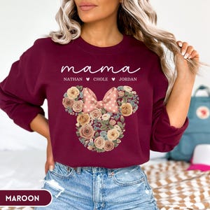 May include: Maroon sweatshirt with the word "mama" in white script, and the names Nathan, Chole, and Jordan below. A floral Minnie Mouse design is in the center, with a pink polka dot bow.