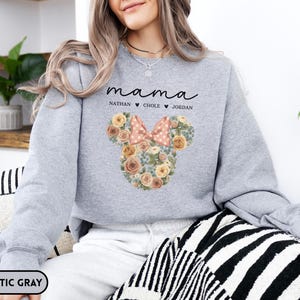 May include: Athletic gray sweatshirt with the word "mama" in script, and the names Nathan, Chole, and Jordan below. A floral Mickey Mouse head design with a pink bow is on the front. The sweatshirt is a comfortable, casual style.