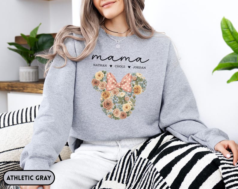 May include: Athletic gray sweatshirt with the word "mama" in script, and the names Nathan, Chole, and Jordan below. A floral Mickey Mouse head design with a pink bow is on the front. The sweatshirt is a comfortable, casual style.
