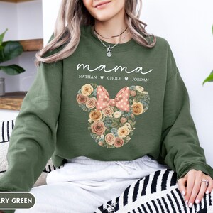May include: Military green sweatshirt with the word "mama" in white script. Below the word "mama" are the names Nathan, Chole, and Jordan. A floral Minnie Mouse design is in the center, with a pink bow.