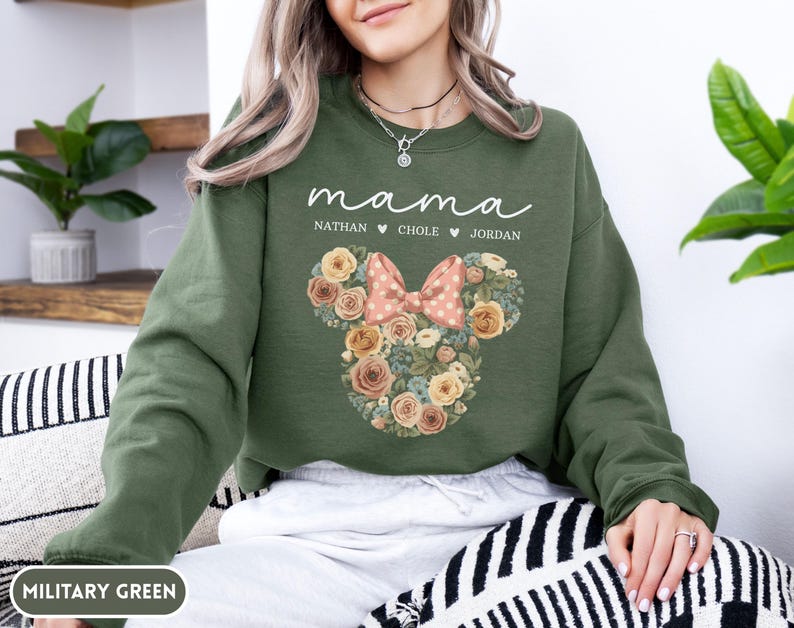 May include: Military green sweatshirt with the word "mama" in white script. Below the word "mama" are the names Nathan, Chole, and Jordan. A floral Minnie Mouse design is in the center, with a pink bow.