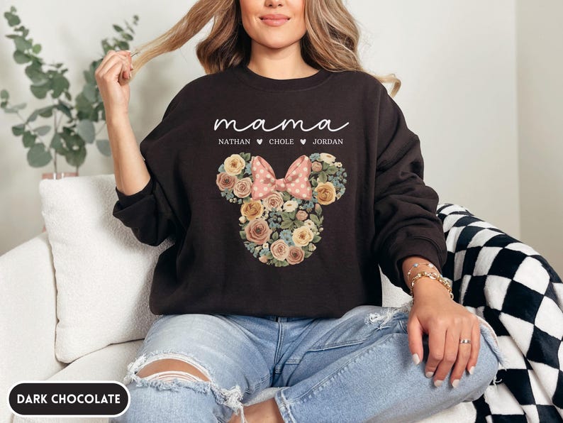 May include: Dark chocolate-colored sweatshirt with the word "mama" in cursive. Below the word "mama" are the names Nathan, Chole, and Jordan. A floral Mickey Mouse head design with a pink bow is on the front.