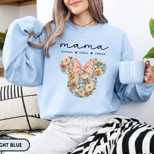 May include: Light blue sweatshirt with the word "mama" in script above a floral Mickey Mouse head design. The design includes a pink bow and the names Nathan, Chole, and Jordan. The words "LIGHT BLUE" are at the bottom.