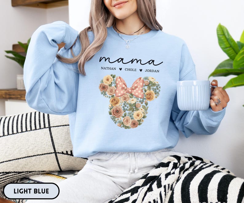 May include: Light blue sweatshirt with the word "mama" in script above a floral Mickey Mouse head design. The design includes a pink bow and the names Nathan, Chole, and Jordan. The words "LIGHT BLUE" are at the bottom.
