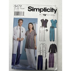May include: A Simplicity 5472 sewing pattern envelope for medical scrubs and lab coats. The front displays illustrations of various scrub tops, trousers, and coats in blue, white, and patterned fabrics, along with a barcode and size range XS, S, M.