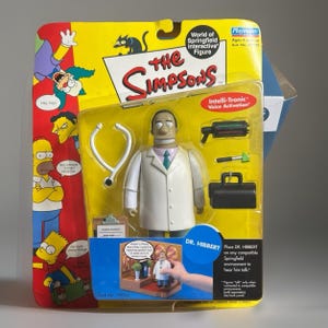 May include: A Dr. Hibbert action figure from The Simpsons World of Springfield series, packaged in a yellow and red blister card. The set includes a white lab coat figure, a stethoscope, a medical bag, a reflex hammer, and a medical device.