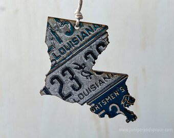 May include: A wooden ornament shaped like the state of Louisiana, decorated with vintage license plates featuring the state name and the number "23".