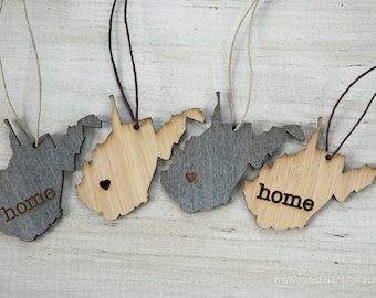 May include: Four wooden ornaments shaped like the state of West Virginia. Two are natural wood with the word "home" engraved on them. The other two are painted gray with a small heart cutout. Each ornament has a string for hanging.