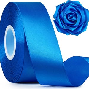 Puede incluir: Una cinta de satén azul real vibrante enrollada en un carrete circular con un núcleo central blanco, acompañada de una sola rosa decorativa de tela hecha del mismo material de satén azul, con pétalos en capas en una disposición circular.