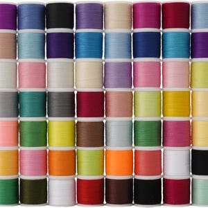 Puede incluir: Una cuadrícula de coloridas bobinas de hilo en varios tonos, incluyendo morado, azul, verde, amarillo, rosa y naranja. Las bobinas están cuidadosamente dispuestas, mostrando una amplia gama de colores para proyectos de costura y manualidades.