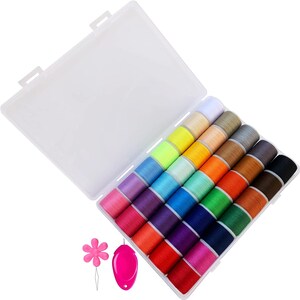 Puede incluir: Un kit de costura de plástico transparente con una variedad de carretes de hilo de colores. Los carretes están dispuestos en filas e incluyen tonos de rosa, morado, azul, verde, amarillo, naranja, marrón y negro. También se incluye un enhebrador de agujas rosa en forma de flor y un soporte para agujas rosa.