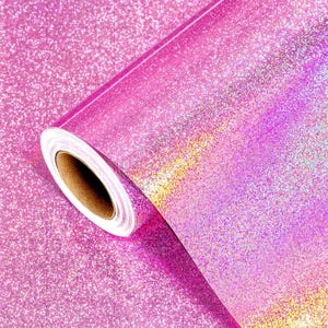 Puede incluir: Un rollo de vinilo rosa con purpurina. El vinilo tiene un acabado brillante e iridiscente con un degradado de colores. El rollo está parcialmente desenrollado, revelando el núcleo de cartón.