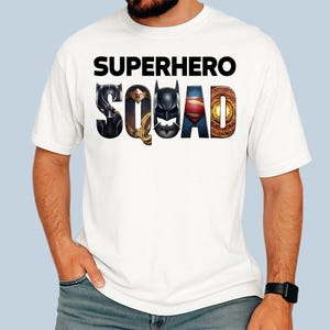 Puede incluir: Camiseta blanca con la frase "SUPERHERO SQUAD" en letras negras. La palabra "SQUAD" est&aacute; dise&ntilde;ada con logotipos de superh&eacute;roes: Pantera Negra, Wonder Woman, Batman, Superman y Doctor Strange.