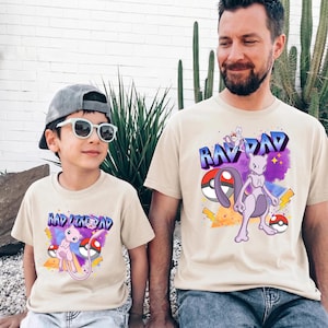 Puede incluir: Dos camisetas beige con gráficos a juego. Una camiseta dice "RAD DAD" con un gráfico morado y blanco de un personaje de Pokémon y una Pokeball. La otra camiseta dice "RAD LIKE DAD" con un gráfico similar.