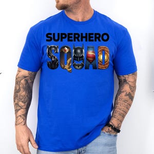 Puede incluir: Camiseta azul real con las palabras "SUPERHERO SQUAD" en negro. La palabra "SQUAD" presenta logotipos de superh&eacute;roes. La camiseta es de manga corta y est&aacute; hecha de un material suave.