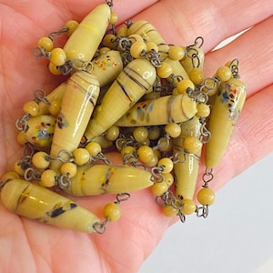 May include: A vintage necklace with light yellow glass beads, elongated and decorated with stripes and colourful accents. The necklace has small, round yellow beads strung on a silver-toned chain. The beads have a unique, handcrafted appearance.