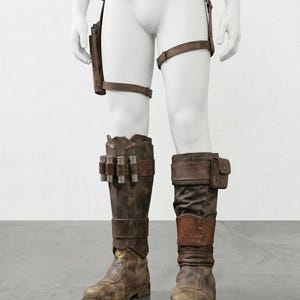 K&ouml;nnte beinhalten: Braunes Lederkost&uuml;m-Set auf einer Schaufensterpuppe. Das Set umfasst einen G&uuml;rtel mit Taschen, eine Halterung, Beingurte und abgenutzte Stiefel. Die Stiefel haben zus&auml;tzliche Taschen und Metallakzente. Das Gesamtbild ist robust und postapokalyptisch.