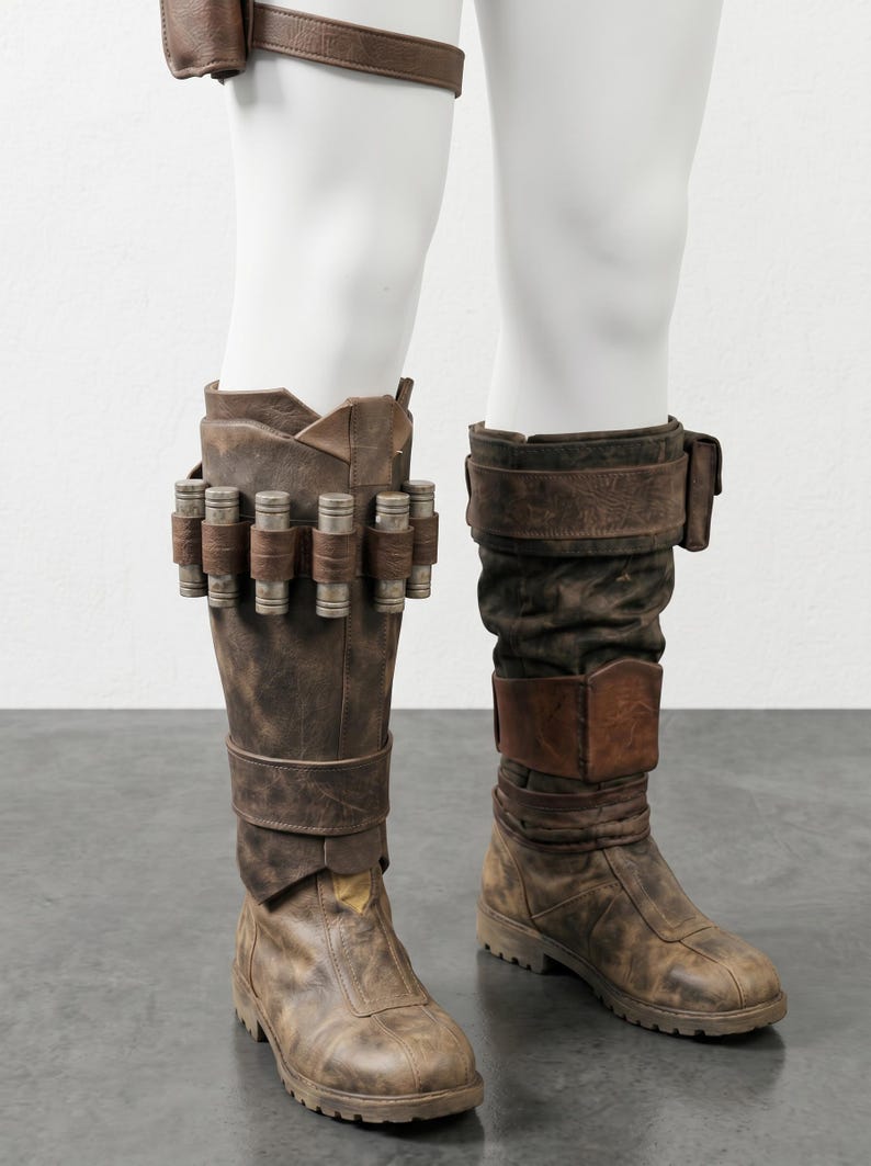 K&ouml;nnte beinhalten: Braune Lederstiefel mit Used-Look, verziert mit dekorativen Metallzylindern und Riemen. Die kniehohen Stiefel haben ein robustes, abgenutztes Aussehen, was auf ein Vintage- oder Kost&uuml;mdesign hindeutet.