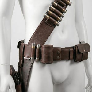 K&ouml;nnte beinhalten: Ein brauner Leder-G&uuml;rtel und Schulterriemen mit Patronenhaltern und Taschen aus Metall. Der G&uuml;rtel hat eine Halterung f&uuml;r eine Schusswaffe. Das Zubeh&ouml;r ist f&uuml;r ein Western- oder Cosplay-Thema konzipiert.