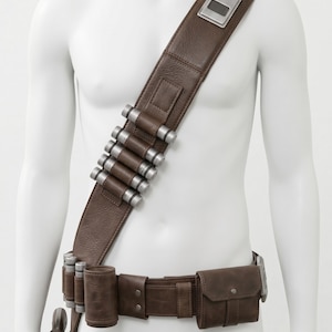 K&ouml;nnte beinhalten: Braunes Leder-Bandolier und G&uuml;rtel-Set mit silberfarbenen Akzenten. Das Bandolier hat einen breiten Riemen mit einer rechteckigen Silberplatte und mehreren silbernen Zylindern. Der G&uuml;rtel enth&auml;lt eine Tasche und ein Holster.