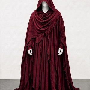 May include: A floor-length, deep burgundy hooded cloak made of textured, lightweight fabric. The garment features a draped cowl neckline, long sleeves, and raw, frayed edges along the hem and front panels, creating a layered, flowing appearance.