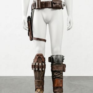 K&ouml;nnte beinhalten: Ein braunes Lederkost&uuml;m-Set, einschlie&szlig;lich eines G&uuml;rtels mit Taschen, einer Halterung und einer Beinr&uuml;stung. Die Stiefel sind braun und abgenutzt. Das Kost&uuml;m wird auf einer Schaufensterpuppe pr&auml;sentiert.