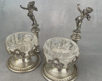 Par de saleros de metal plateado rematados por un delicado querubín/putti