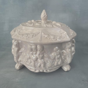 Bombonera grande de cerámica rosa iridiscente con decoración de querubines y putti, lata de galletas barroca vintage de ~19 cm.