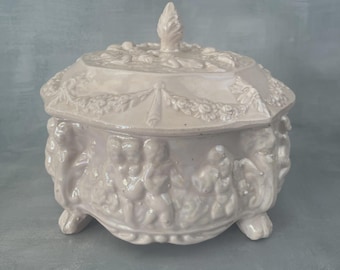 Bombonera grande de cerámica rosa iridiscente con decoración de querubines y putti, lata de galletas barroca vintage de ~19 cm.