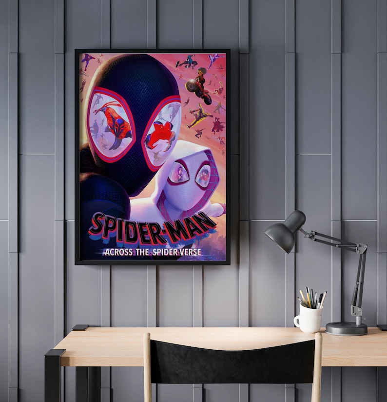 May include: Framed poster featuring Spider-Man characters from the movie "Across the Spider-Verse." The artwork showcases Miles Morales and Spider-Gwen, with a vibrant, action-packed design. The poster is displayed on a gray wall above a wooden desk.