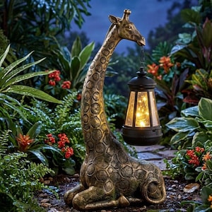 Può includere: Una scultura di giraffa color bronzo in posizione di riposo, caratterizzata da un motivo a macchie testurizzato. La giraffa tiene in bocca una lanterna nera contenente luci a corda calde che illuminano l'area circostante.