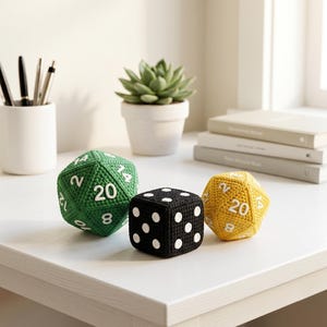 Può includere: Un set di tre dadi all'uncinetto che include un dado verde a venti facce con numeri bianchi, un dado nero a sei facce con punti bianchi e un dado giallo a venti facce con numeri bianchi, tutti realizzati con una trama in filato.