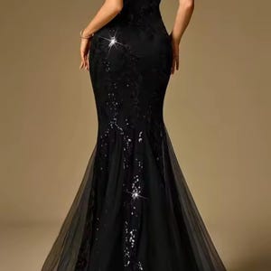 Puede incluir: Un vestido de noche negro con cuello halter y silueta de sirena. El vestido presenta intrincados detalles de lentejuelas y encaje, y una falda de tul fluida. La parte trasera del vestido es visible.