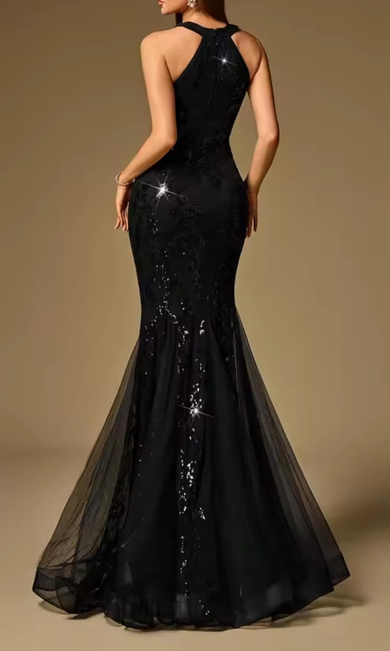 Puede incluir: Un vestido de noche negro con cuello halter y silueta de sirena. El vestido presenta intrincados detalles de lentejuelas y encaje, y una falda de tul fluida. La parte trasera del vestido es visible.