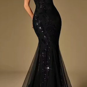Puede incluir: Un vestido de noche negro con cuello halter, corpi&ntilde;o ajustado y falda larga y fluida. El vestido presenta adornos de lentejuelas y una capa transparente en el dobladillo. El dise&ntilde;o elegante es adecuado para eventos formales.