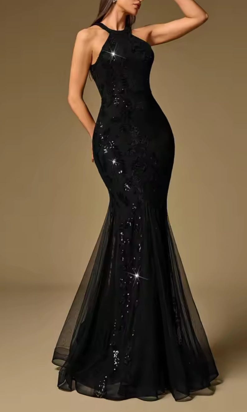 Puede incluir: Un vestido de noche negro con cuello halter, corpi&ntilde;o ajustado y falda larga y fluida. El vestido presenta adornos de lentejuelas y una capa transparente en el dobladillo. El dise&ntilde;o elegante es adecuado para eventos formales.