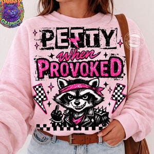 May include: Pink sweatshirt with the text "PETTY when PROVOKED" and a graphic of a raccoon wearing a bandana and leather jacket. The raccoon is giving the middle finger. The design includes lightning bolts and stars.