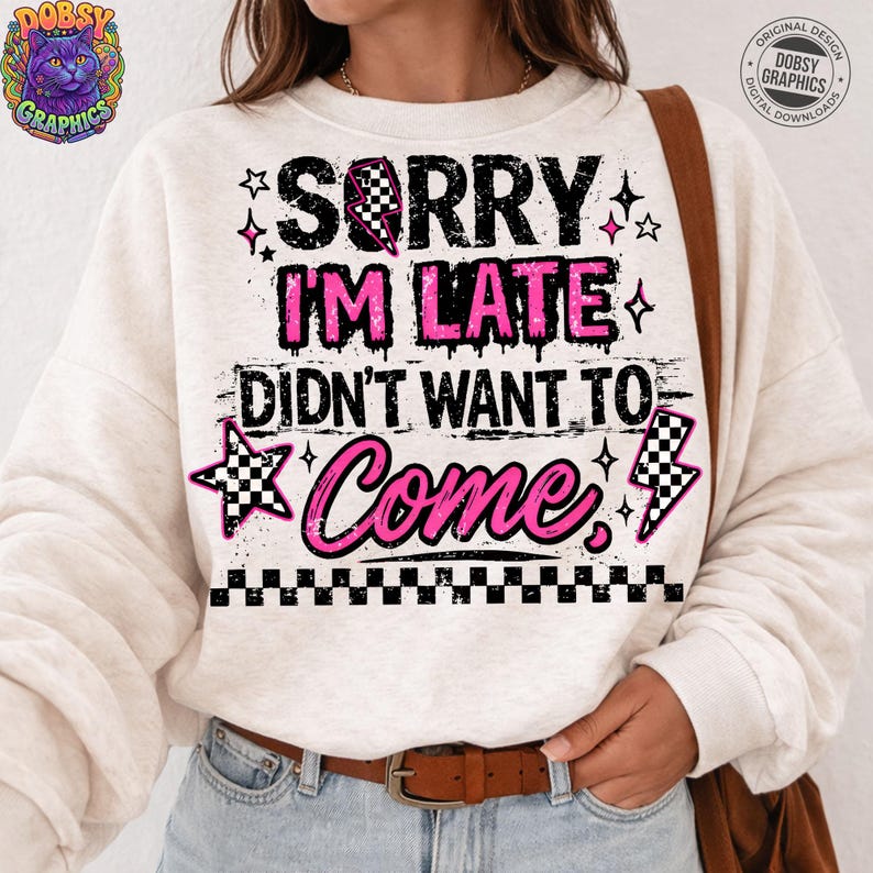 May include: A cream-colored sweatshirt with the text "SORRY I'M LATE DIDN'T WANT TO Come" in black and pink. The design includes stars, a checkered flag, and a lightning bolt graphic.