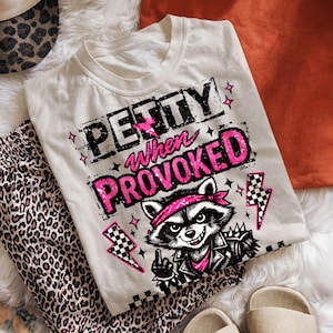 May include: Off-white t-shirt with the text "Petty When Provoked" in black and pink. The shirt features a raccoon graphic wearing a bandana and a leather jacket. Leopard print pants and a leopard print hat are also visible.